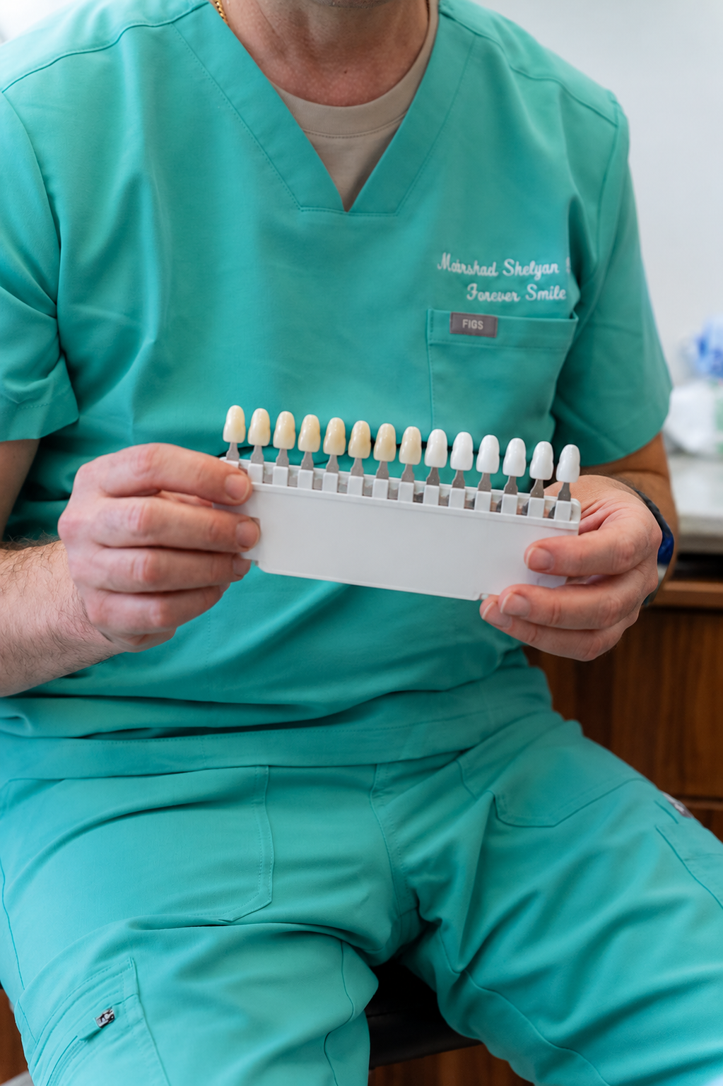Dentist in teal scrubs holding a shade guide for matching tooth color