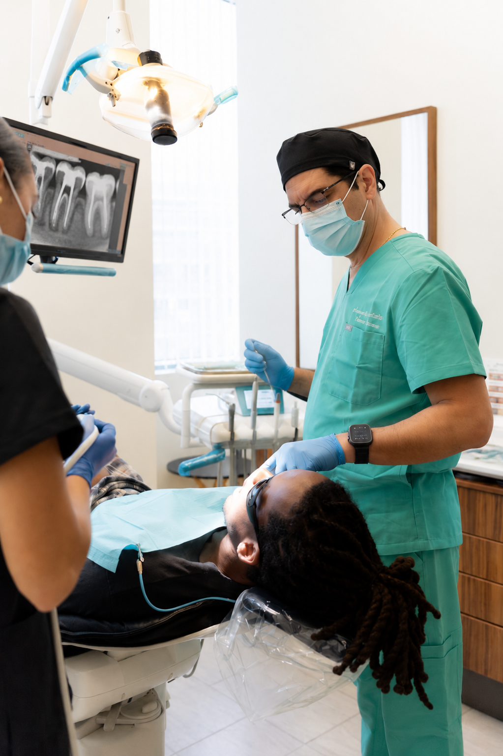 Dentist treating a patient in a dental chair while viewing X-rays on a monitor