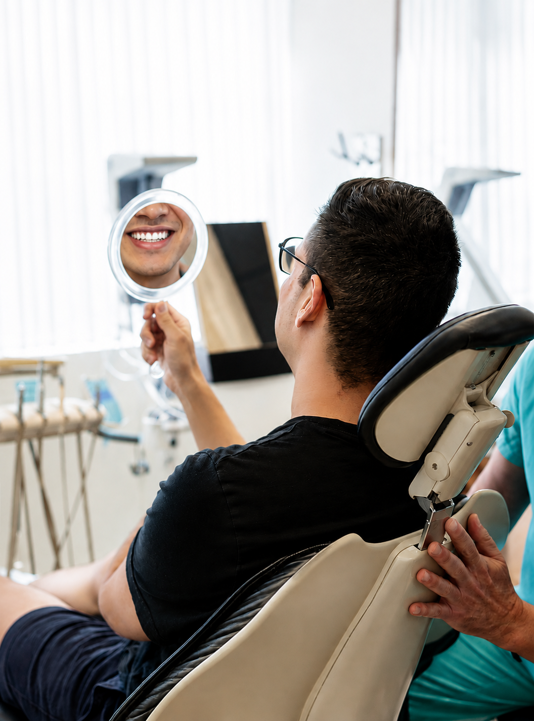 Person in a dental chair holding a mirror at a smiling mouth in a clinic