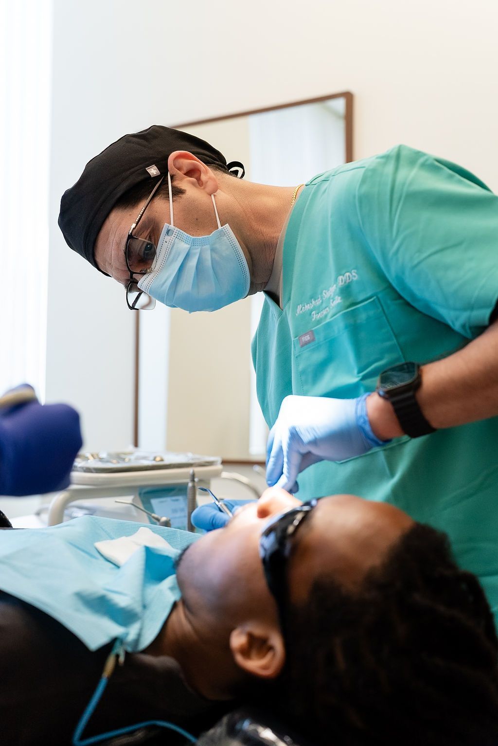 Dentist in green scrubs and mask examining a patient in a dental chair