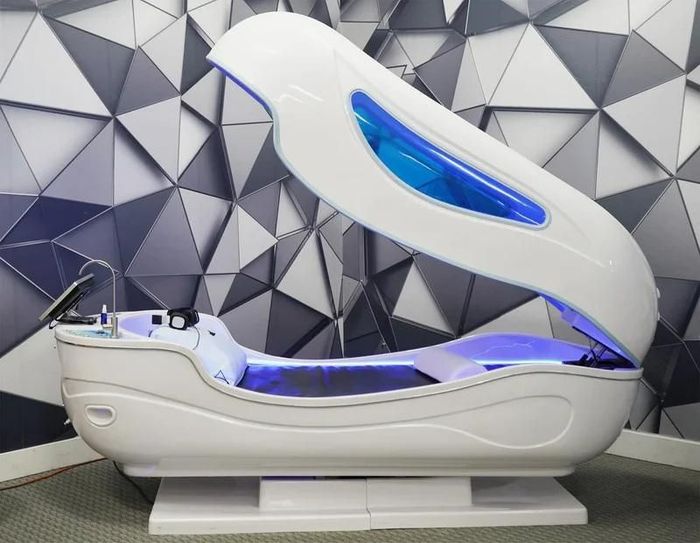 Beige electric massage chair in a minimalist room, with a small vase on a shelf behind it.