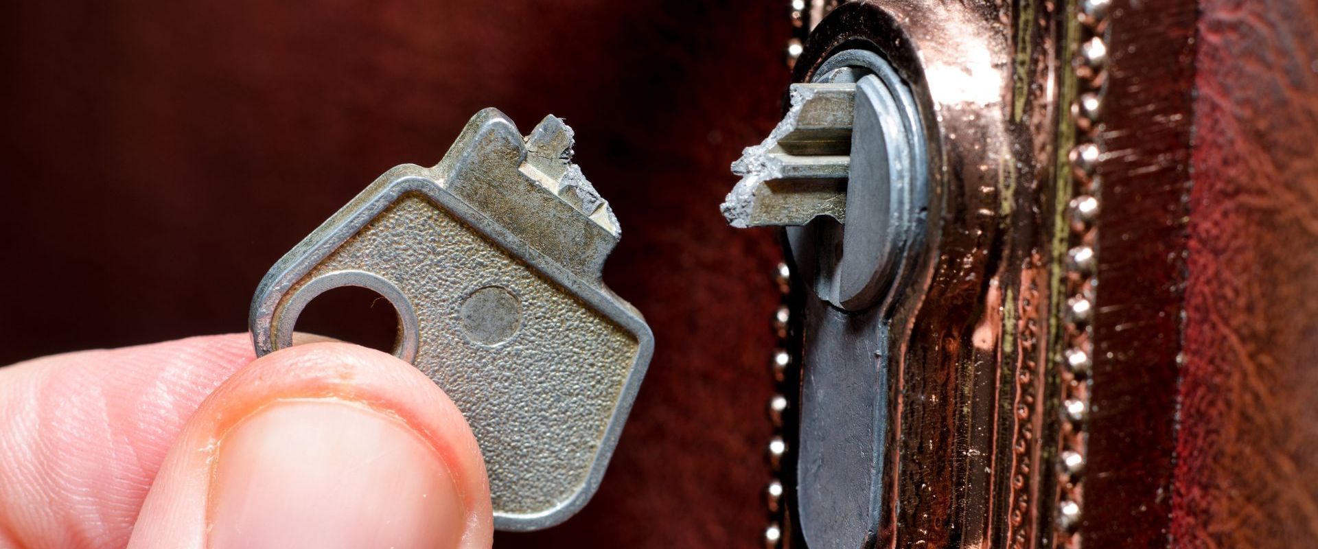A person is holding a broken key in front of a door lock.