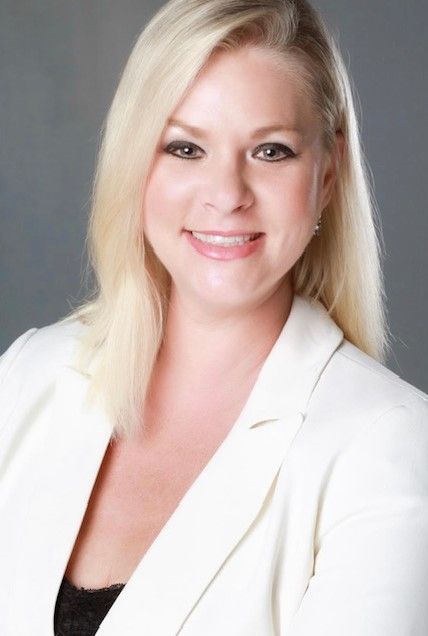 A smiling blonde person wearing a white blazer against a gray background.