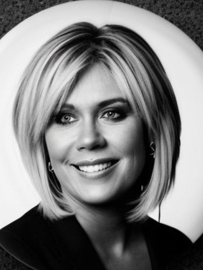 A black-and-white portrait of a smiling person with a layered bob haircut, wearing a blazer against a circular backdrop.