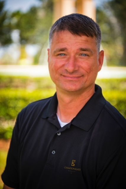 Man with graying hair in black polo shirt smiles outdoors.