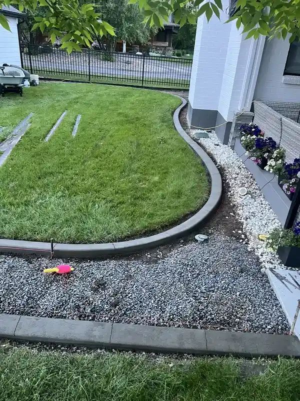 Curved front yard with grass, gravel border, and flower bed beside a house.