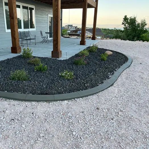 Curved gravel landscape bed with small plants beside a house patio and columns