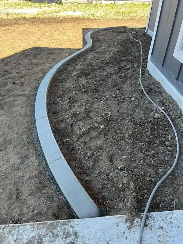 Curved metal landscape edging outlining a dirt bed beside a house, with a hose running along the soil.