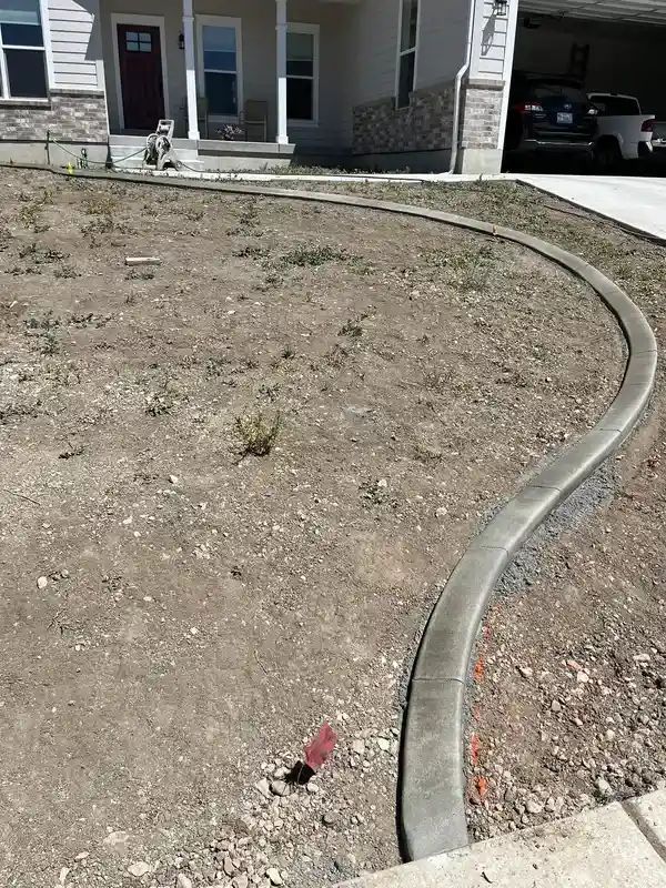Curved concrete edging around a bare front yard beside a house and driveway