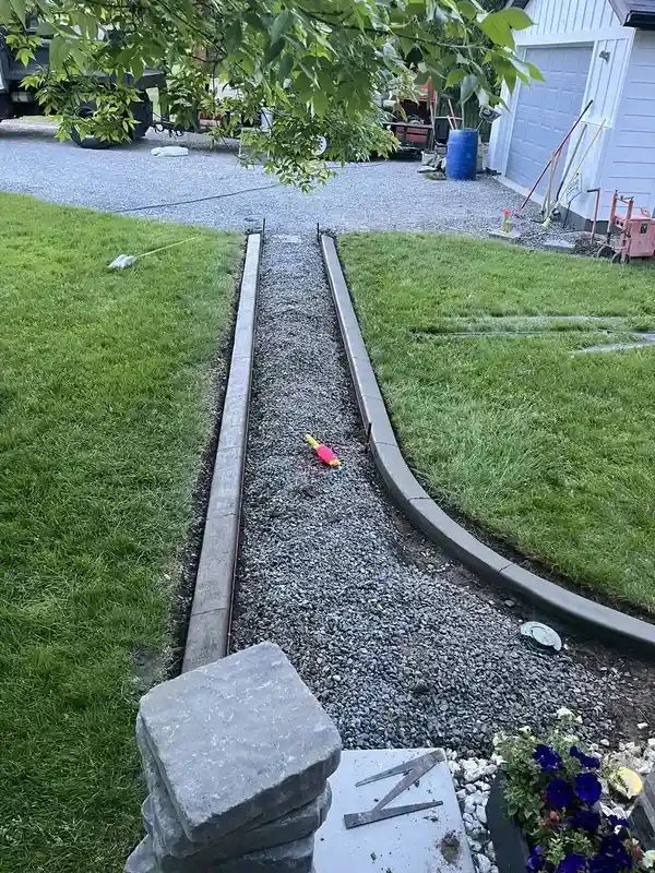 Gravel garden path between green lawns leading to a driveway beside a house, with flowers in the foreground.