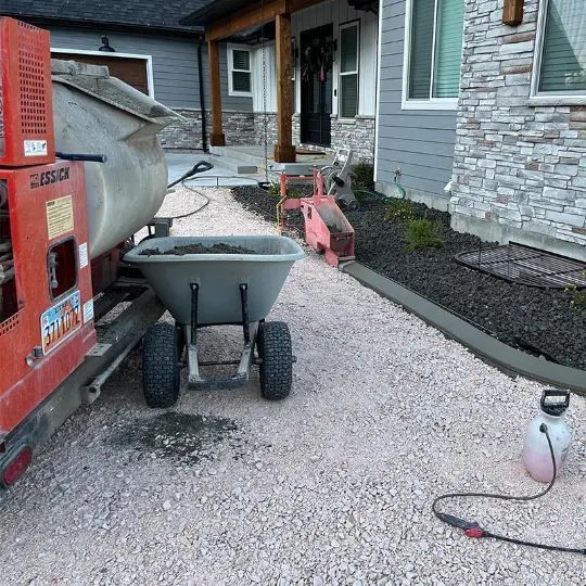 Gravel driveway with wheelbarrow and red construction machine beside a house under renovation.
