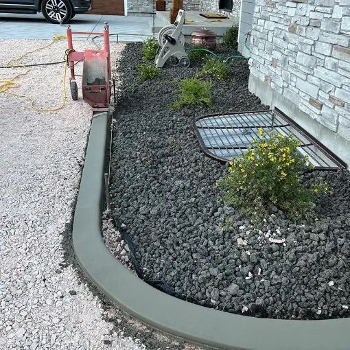 Landscaped curb with gray rocks, small shrubs, and a red wheelbarrow beside a stone house