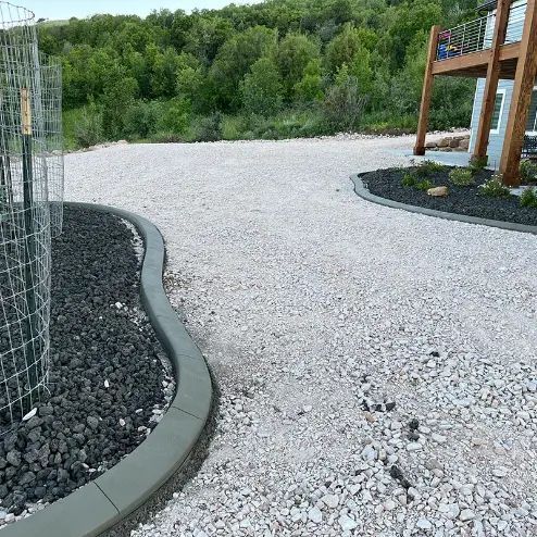 Curved gravel path beside black rock landscaping and wooden deck railings in a green garden