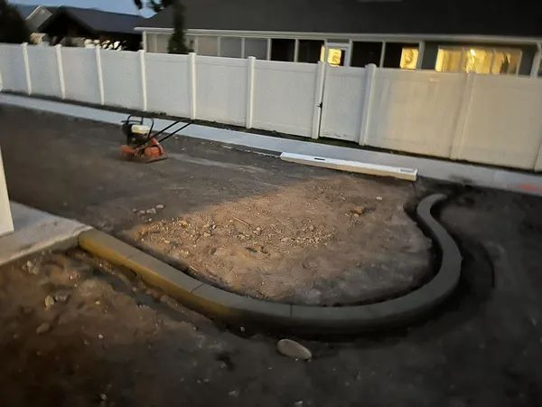 Construction site with curved black hose around a dirt patch beside a white fence at dusk