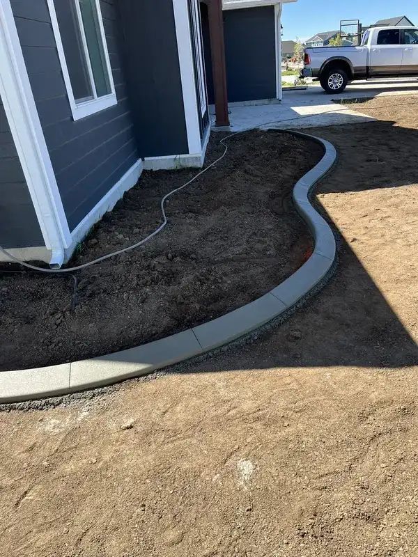 Newly landscaped curved concrete border beside a house with bare soil and a parked truck in the background