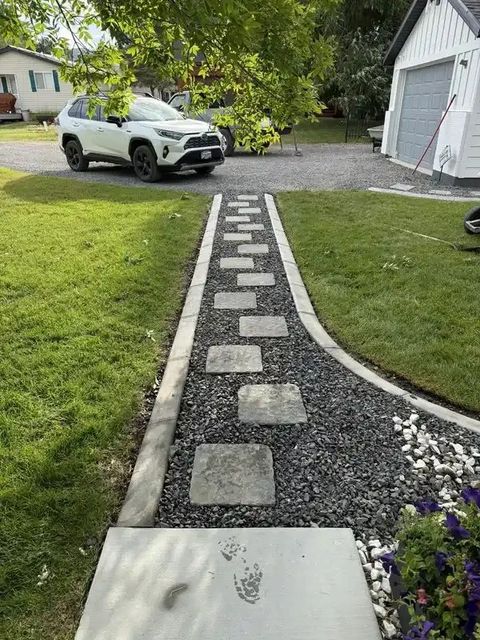 Curved stone garden path with stepping stones leading to a driveway and white SUV beside a house