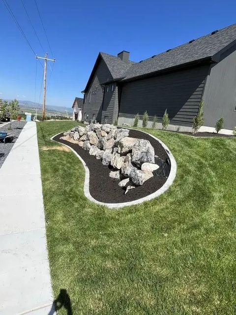 Curved rock garden with black edging beside a sidewalk and dark house on a sunny residential street