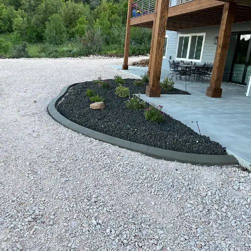 Curved black mulch bed with small plants beside a concrete patio and wooden porch posts