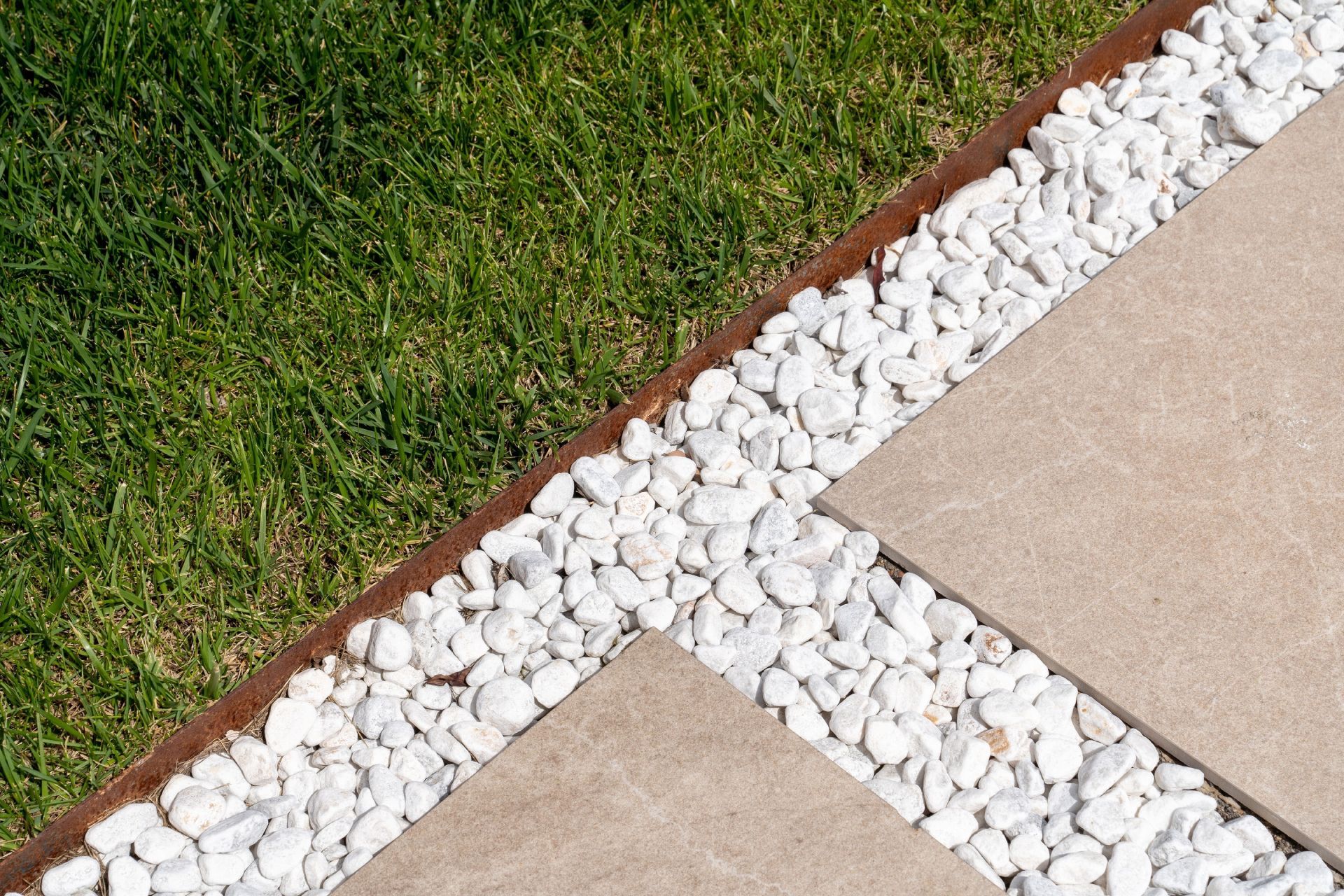 Grass bordered by white gravel edging between tan paved slabs