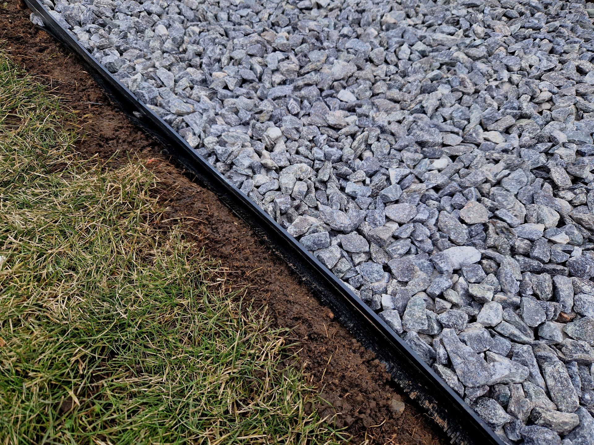 Gravel path edged with black landscape border beside green grass.