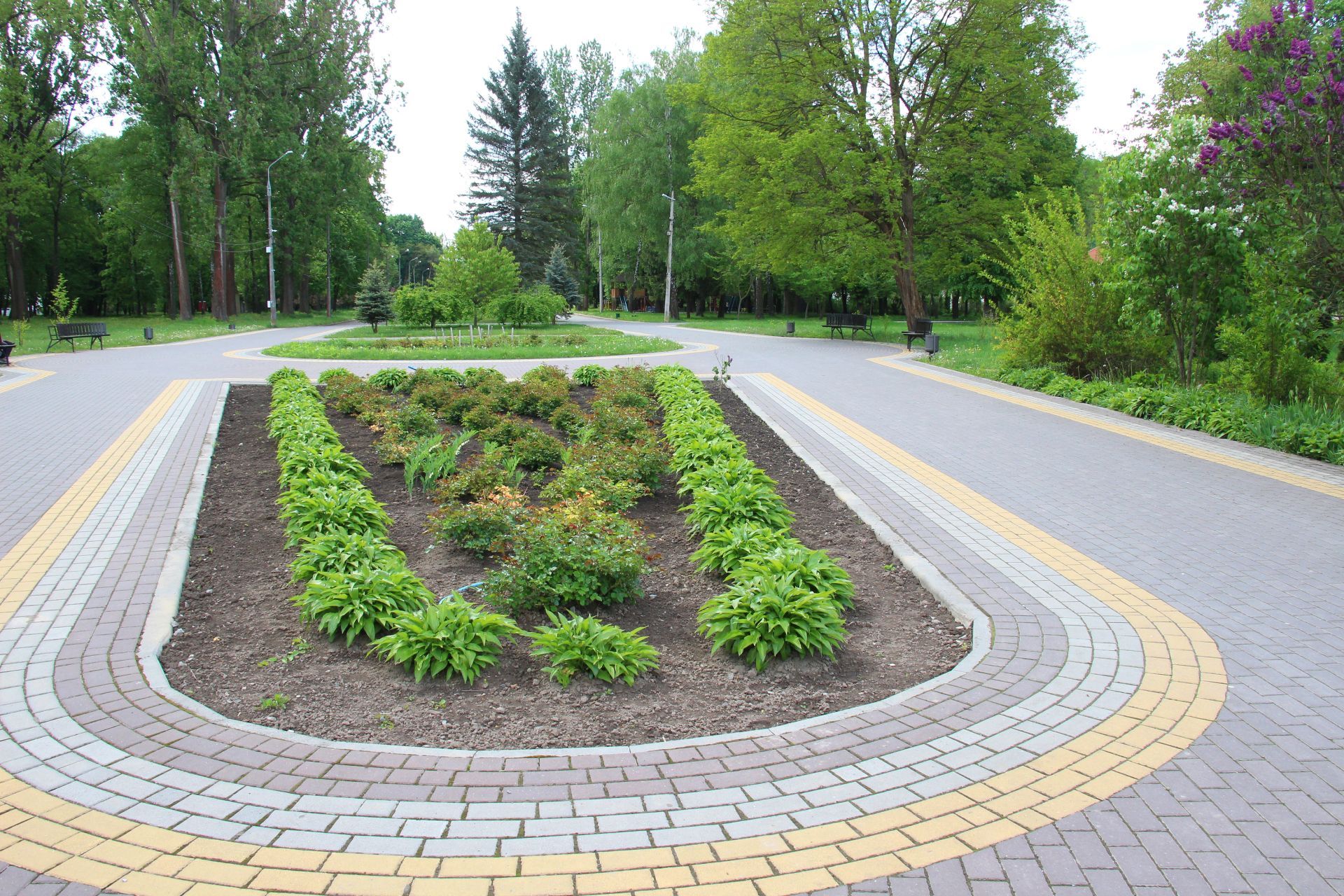 Curved brick walkway around a landscaped flower bed in a green park.