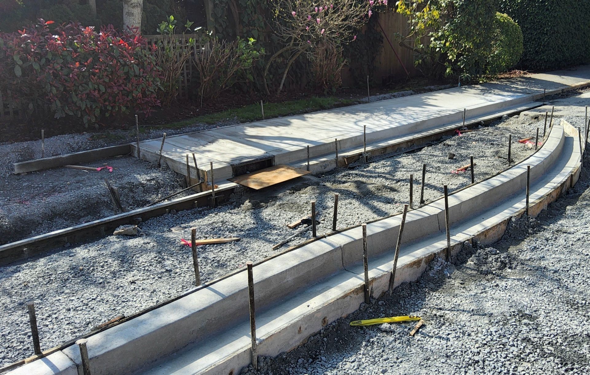 Curved concrete walkway under construction with gravel, wooden forms, and stakes