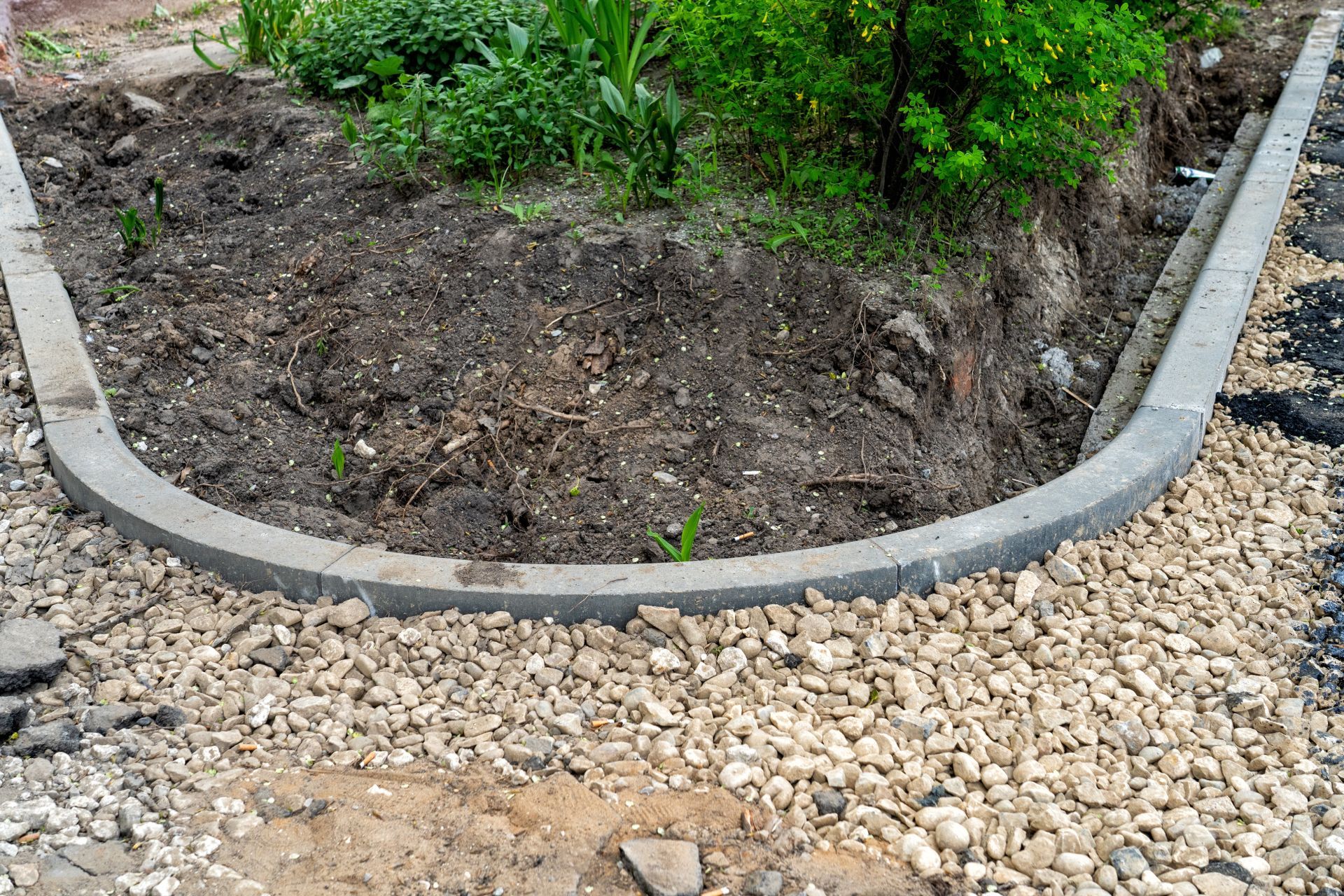 Curved concrete edging around a mulched garden bed with green shrubs and gravel path