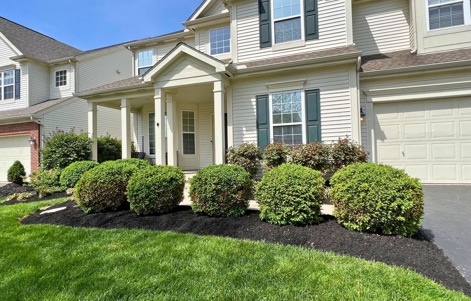 Suburban house with white siding, front porch, garage, and trimmed shrubs along the walkway