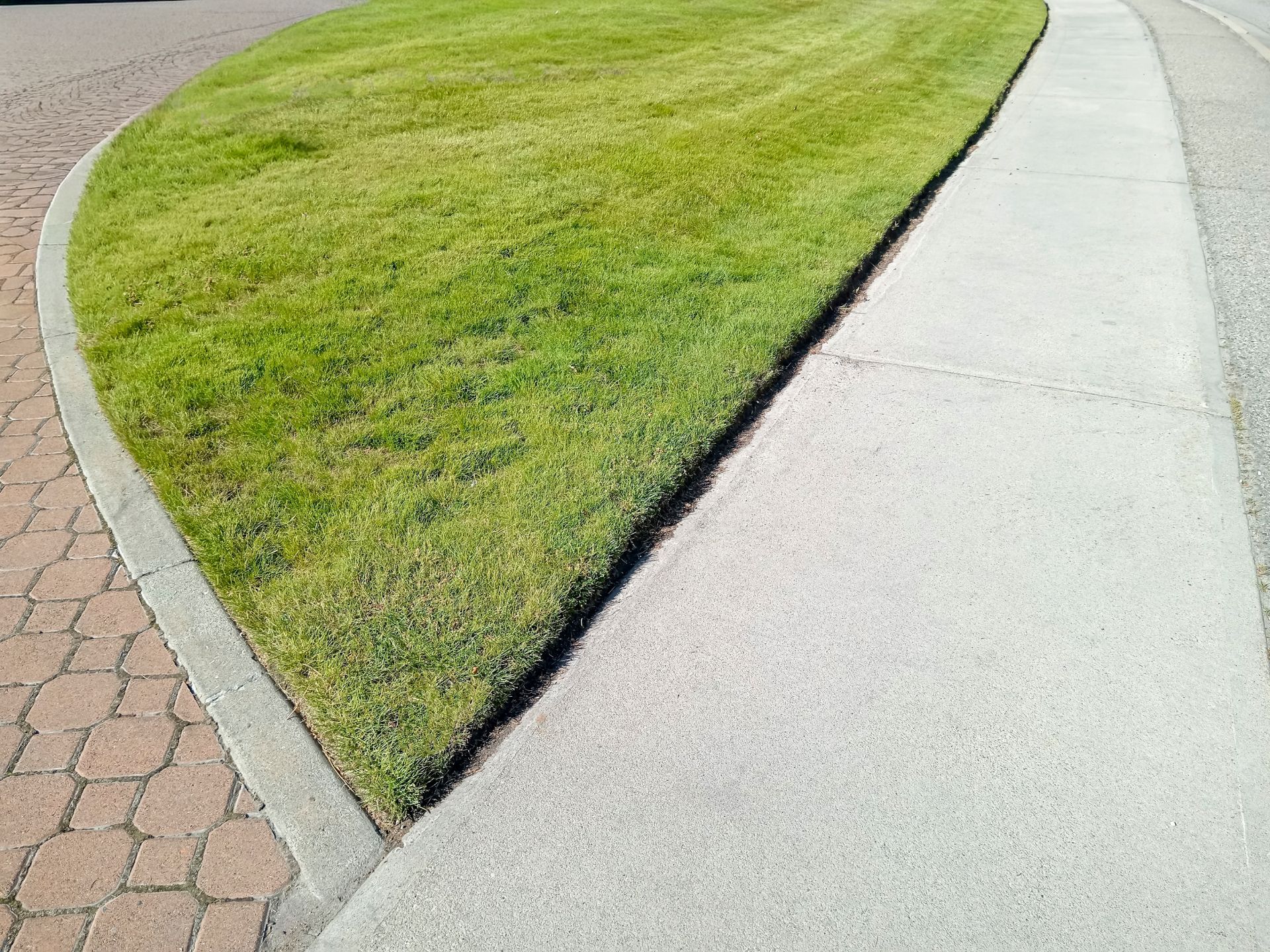 Curved grass median bordered by a sidewalk and paved walkway
