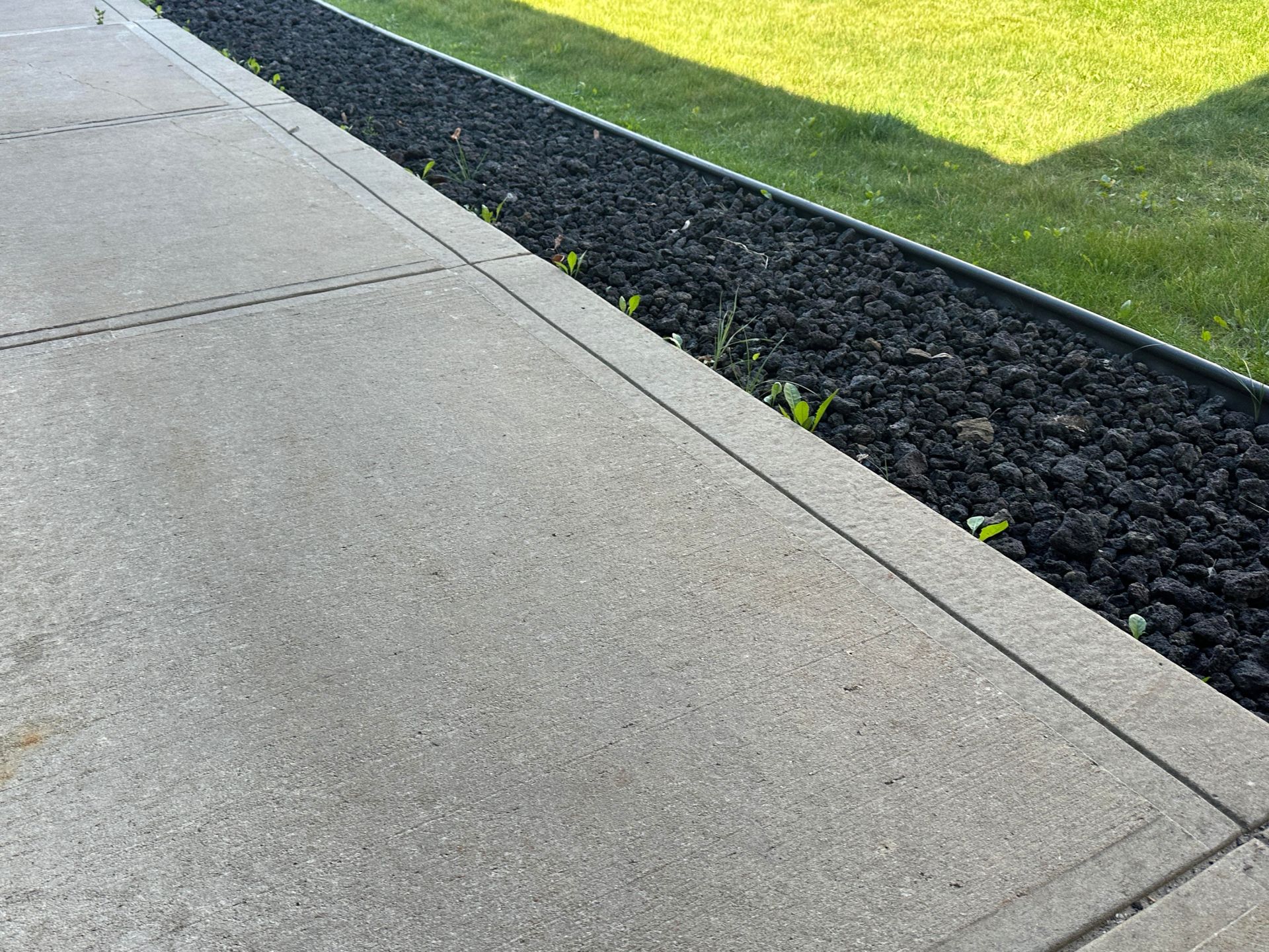 Concrete sidewalk beside black mulch and green grass lawn