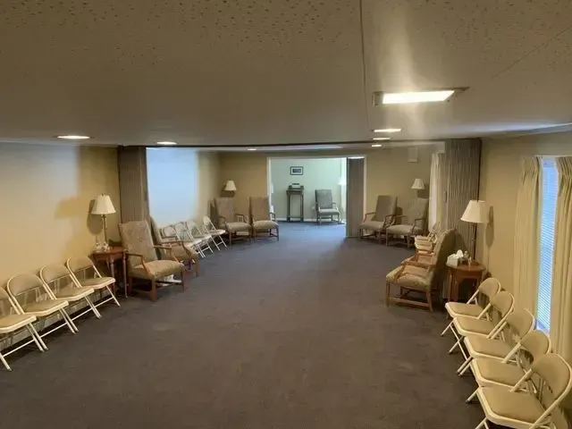 Empty waiting room with beige walls, rows of chairs, a lamp, and a carpeted floor