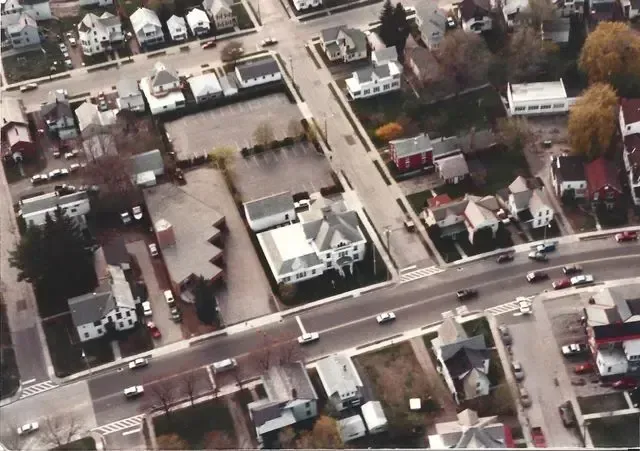 Aerial view of a suburban neighborhood with houses, trees, and cars on intersecting roads.
