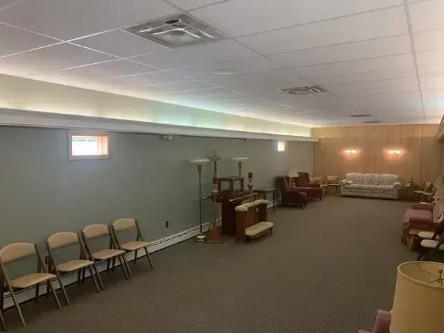 Empty community room with folding chairs, tables, and a carpeted floor under fluorescent lighting