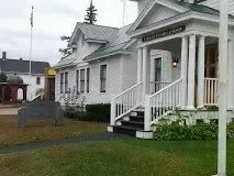 White house with porch and steps beside a grassy yard on an overcast day