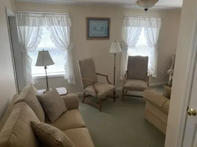 Cozy beige living room with sofas, chairs, lamps, and sheer-curtained windows