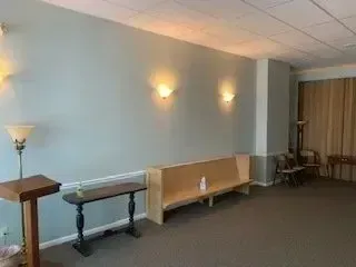 Empty hallway with wall sconces, a side table, bench, and chairs near curtained windows.