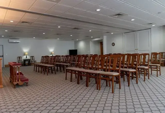 Empty banquet hall with rows of wooden chairs and tables under bright ceiling lights