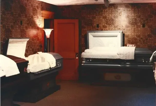 Two made beds in a dim brick-walled room with a red door and warm lamp light