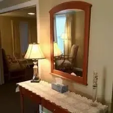 Lamp on a hallway table beneath a framed mirror, with a tissue box and decorative vase.