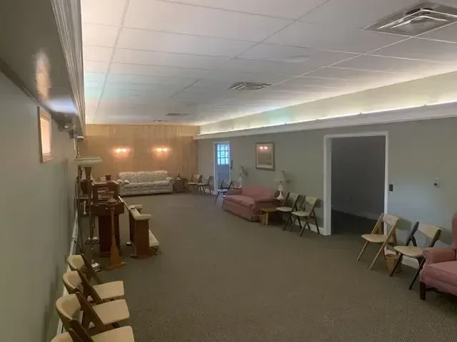 Large empty community room with chairs along the walls, a piano, and soft ceiling lighting.