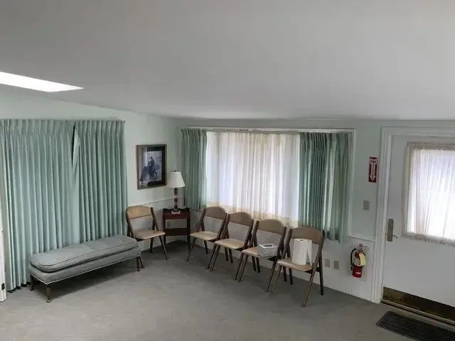 Waiting room with rows of chairs, a green bench, curtained windows, and a fire extinguisher on the wall