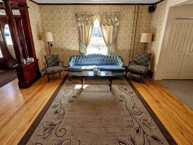 Living room with sofa, two chairs, large rug, and tall windows with curtains