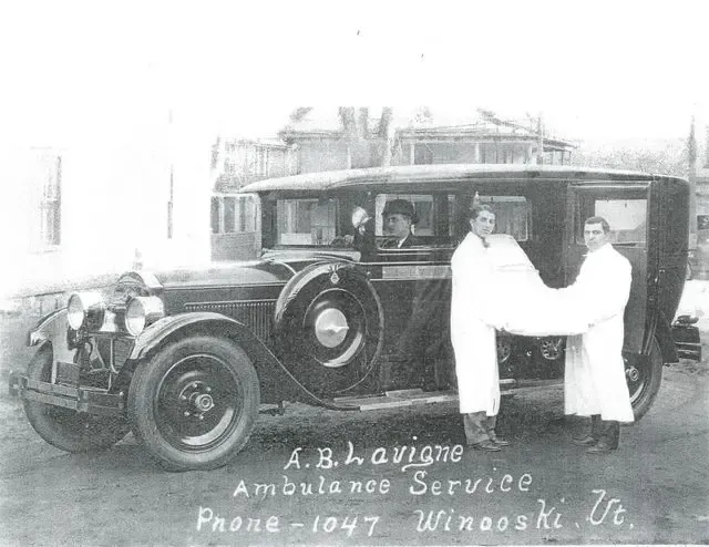 Vintage ambulance with two attendants beside it, labeled “A.B. A. Vioing Ambulance Service” and a phone number.