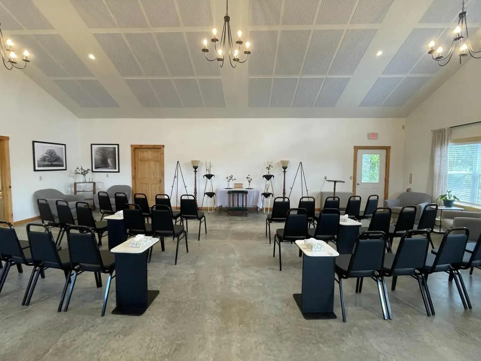 Bright meeting room with rows of black chairs facing a front stage with microphones and instruments