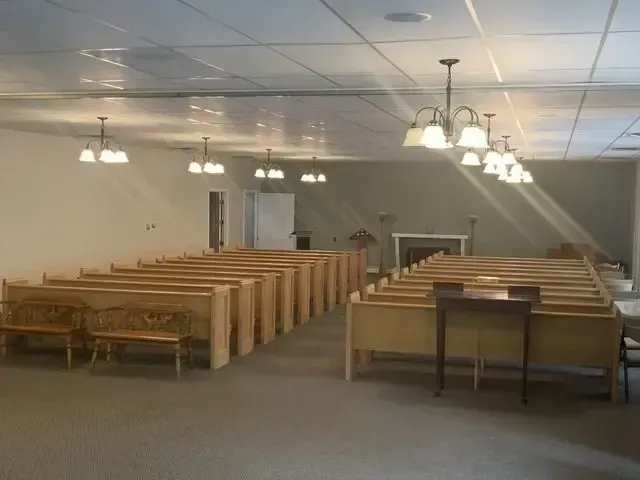 Empty church sanctuary with rows of wooden pews and hanging lights under a tiled ceiling