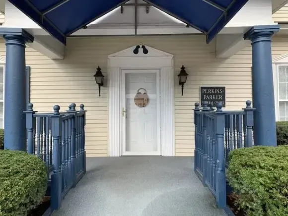 Front porch with blue railings and columns, white door, and small signs on either side.
