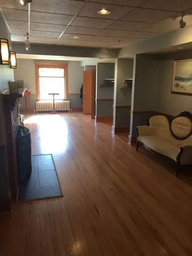 Empty waiting room with wood floors, white walls, a fireplace, and a sunlit window at the far end
