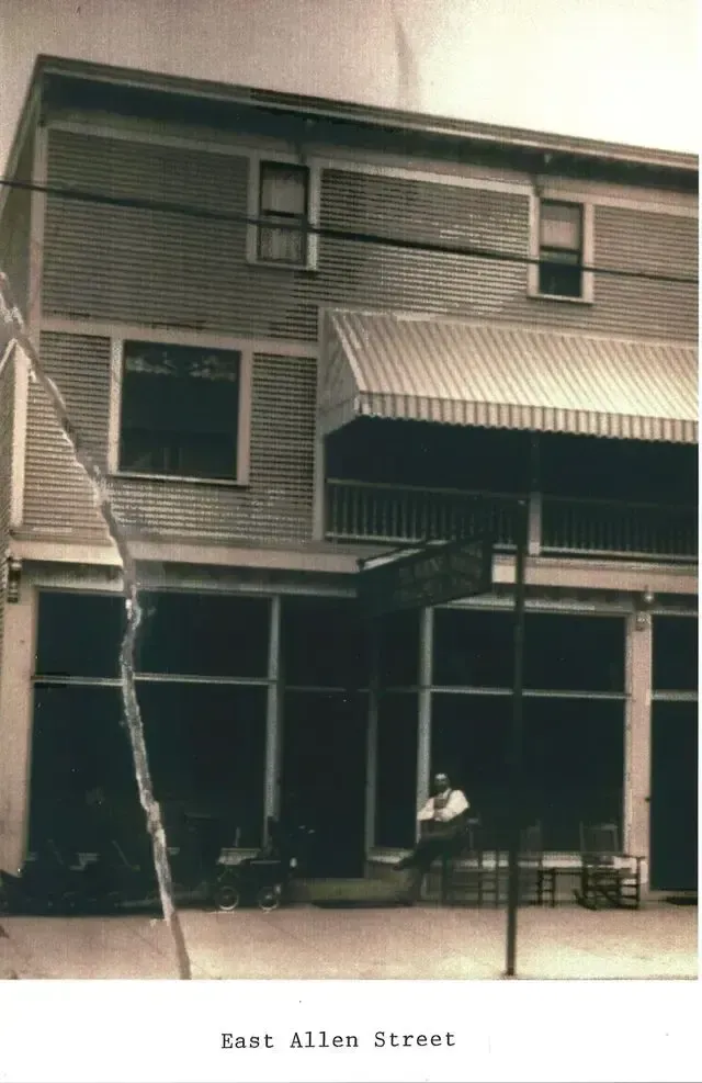 Historic storefront on East Allen Street with awnings and a person seated outside under the porch