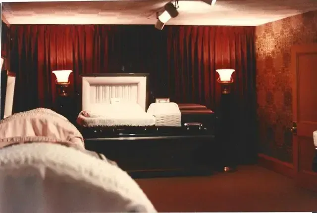Dim bedroom with a large bed, red curtains, wall sconces, and a warm, moody glow.