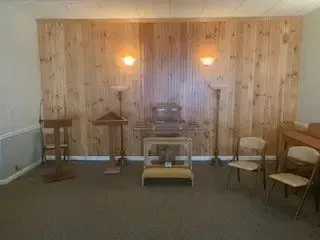 Wood-paneled room with two wall lights, small tables, chairs, and a central table on a carpeted floor